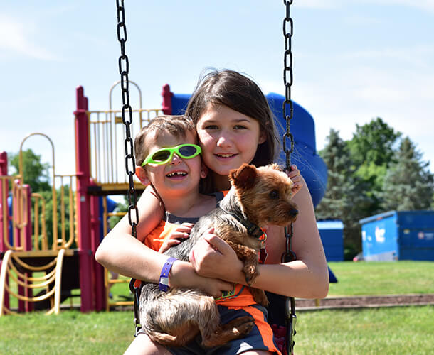 a young girl and boy and their dog on a swing in a manufactured home community park